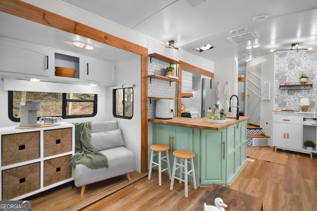 kitchen with green cabinetry, butcher block countertops, decorative backsplash, white cabinets, and light wood-type flooring