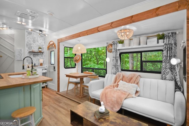 living room featuring light hardwood / wood-style floors, crown molding, sink, and an inviting chandelier