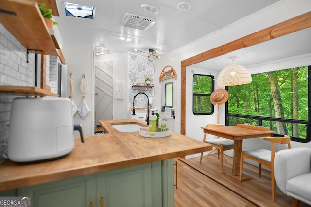 kitchen featuring pendant lighting, sink, light hardwood / wood-style flooring, green cabinetry, and ornamental molding