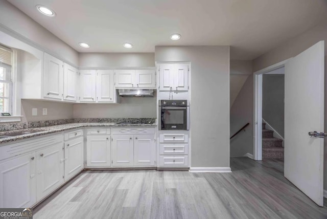 kitchen with black oven, light stone counters, white cabinets, and light wood-type flooring