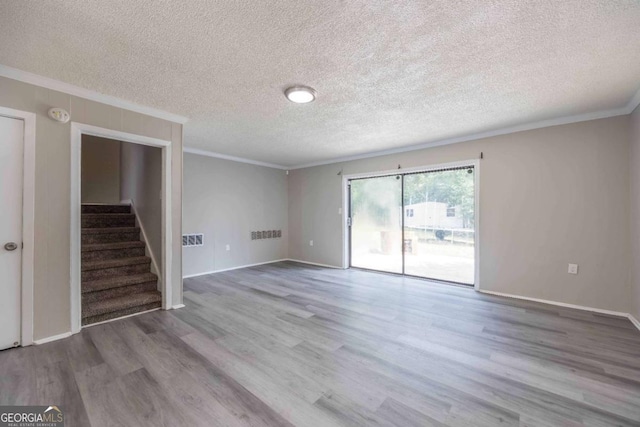 empty room with light wood-type flooring, a textured ceiling, and ornamental molding