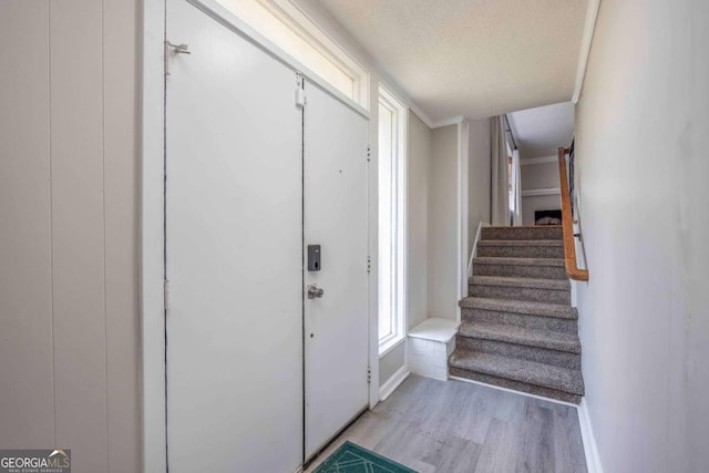 foyer featuring light hardwood / wood-style floors, ornamental molding, and a textured ceiling