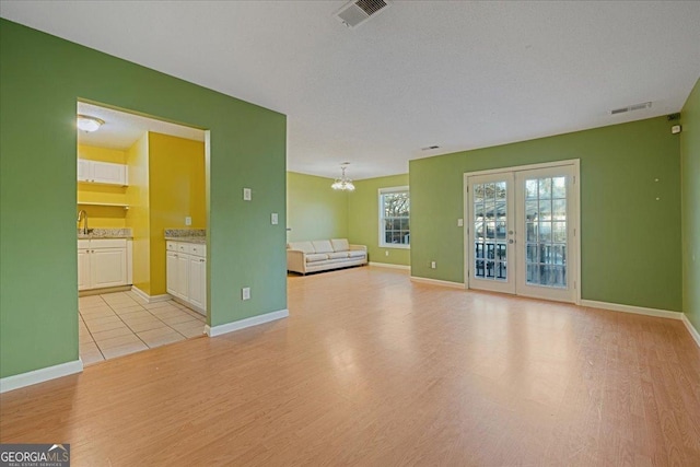 interior space with french doors, a textured ceiling, light hardwood / wood-style floors, and a notable chandelier