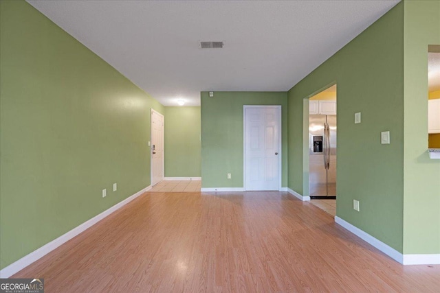 empty room with light wood-type flooring, baseboards, and visible vents