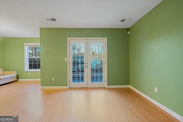 unfurnished room with a textured ceiling, french doors, plenty of natural light, and light wood-type flooring