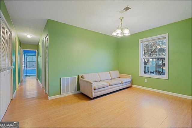 living area with light hardwood / wood-style floors, a textured ceiling, and a notable chandelier