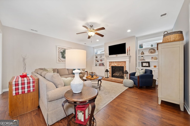 living room with ceiling fan, dark hardwood / wood-style flooring, built in features, and a fireplace