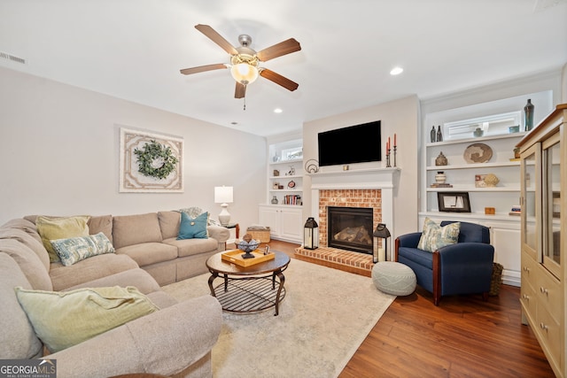 living room featuring ceiling fan, wood-type flooring, built in features, and a brick fireplace