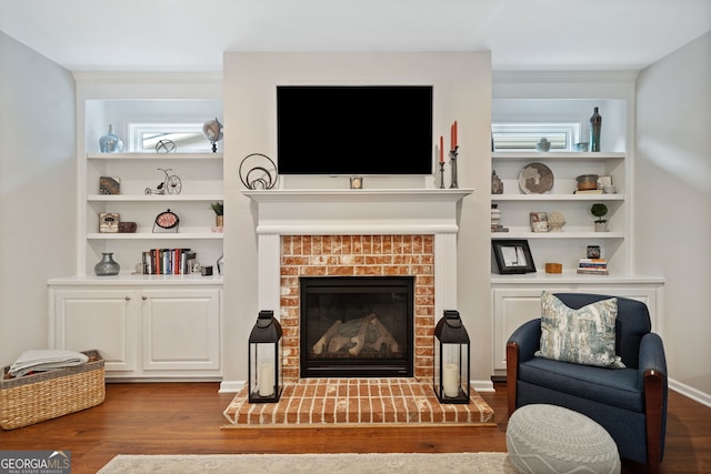 living room with built in shelves, hardwood / wood-style floors, and a brick fireplace