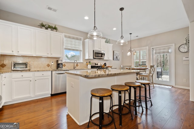 kitchen featuring white cabinetry, a center island, stainless steel appliances, dark hardwood / wood-style floors, and decorative light fixtures