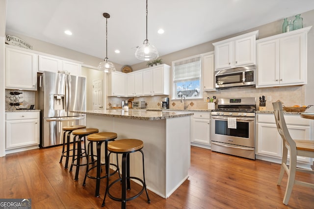 kitchen featuring decorative light fixtures, a center island, stainless steel appliances, and white cabinetry