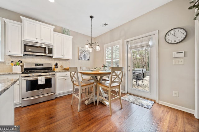 kitchen with decorative backsplash, appliances with stainless steel finishes, light stone counters, dark hardwood / wood-style floors, and white cabinetry