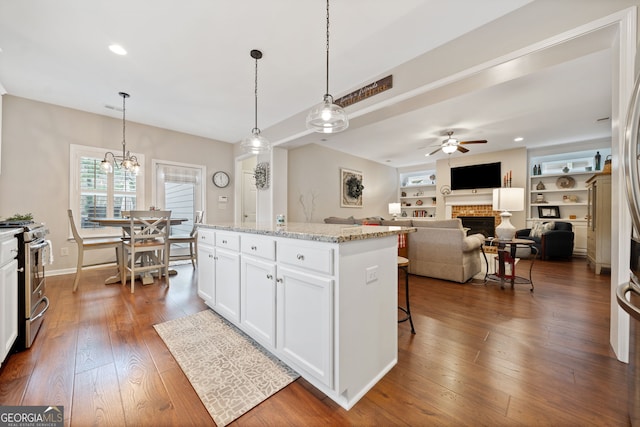 kitchen featuring a center island, stainless steel gas range, light stone counters, decorative light fixtures, and white cabinets