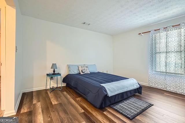 bedroom featuring multiple windows, dark wood-type flooring, and a textured ceiling