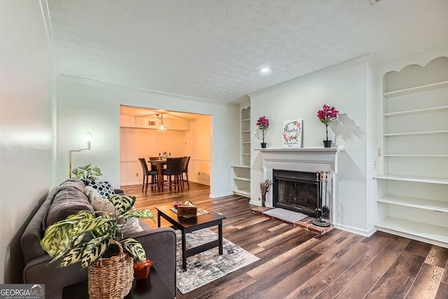 living room featuring built in features, dark wood-type flooring, a textured ceiling, and ornamental molding