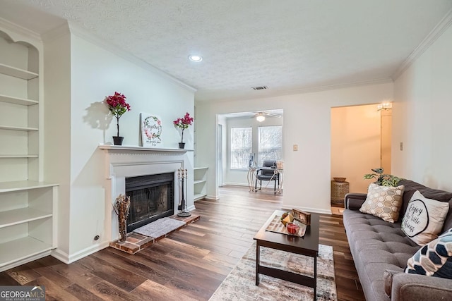 living room featuring built in shelves, dark hardwood / wood-style floors, ornamental molding, and a textured ceiling