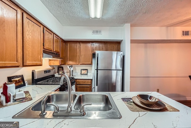 kitchen featuring stainless steel refrigerator, light stone countertops, gas range, and a textured ceiling