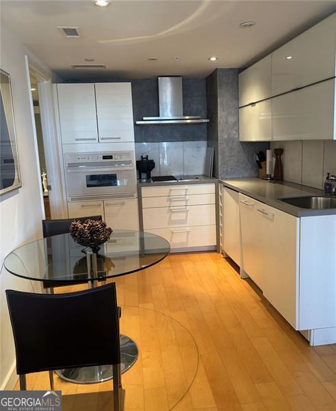 kitchen featuring white cabinetry, wall chimney range hood, sink, and oven