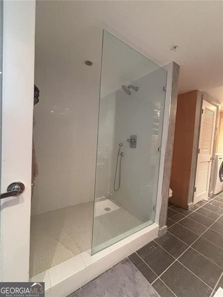 bathroom featuring tiled shower, toilet, washer / dryer, and tile patterned flooring