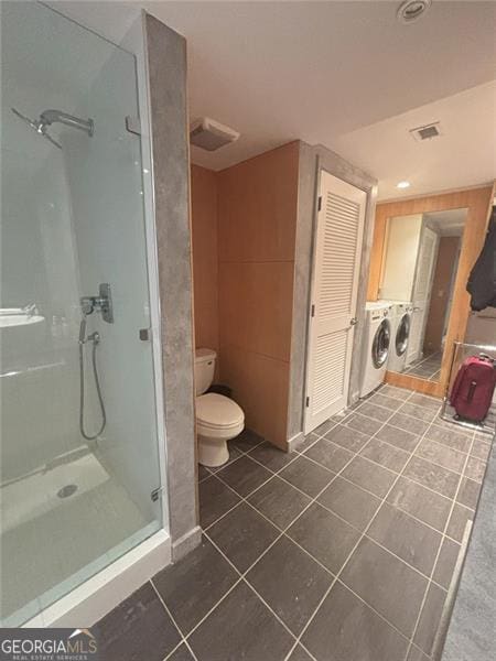 bathroom featuring washing machine and clothes dryer, toilet, tile patterned flooring, and a shower