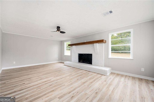 unfurnished living room featuring a textured ceiling, light hardwood / wood-style floors, a brick fireplace, and ceiling fan