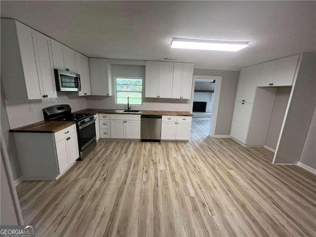 kitchen featuring sink, butcher block countertops, appliances with stainless steel finishes, white cabinets, and light wood-type flooring