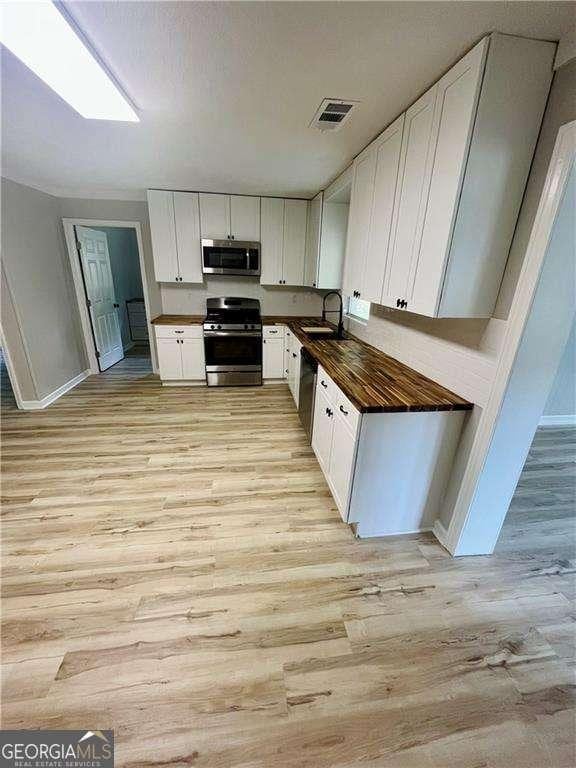 kitchen with sink, white cabinetry, stainless steel appliances, and light wood-type flooring