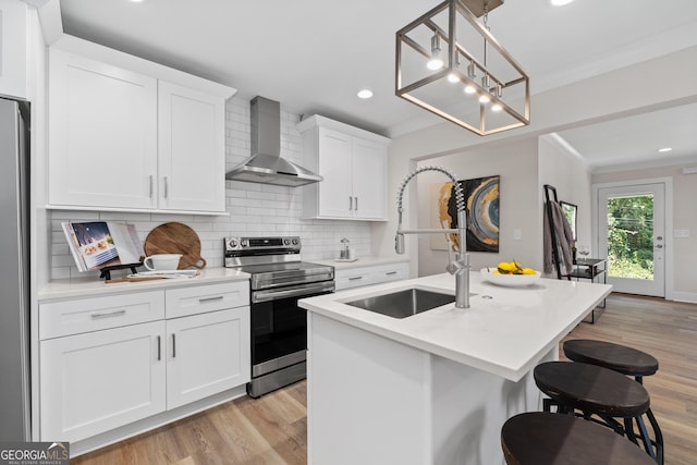 kitchen with wall chimney exhaust hood, a kitchen island with sink, decorative light fixtures, white cabinetry, and stainless steel electric range