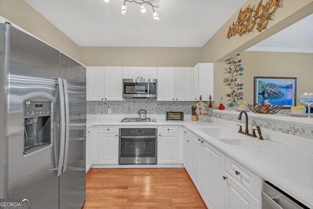 kitchen with sink, stainless steel dishwasher, light hardwood / wood-style floors, decorative light fixtures, and white cabinets