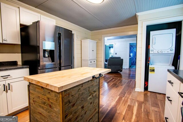 kitchen featuring dark wood-type flooring, wooden counters, stainless steel refrigerator with ice dispenser, white cabinetry, and stacked washer / dryer