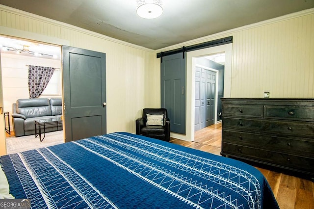 bedroom with a barn door, hardwood / wood-style flooring, a closet, and crown molding