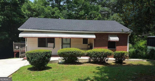 view of front of house with brick siding, a front yard, and roof with shingles