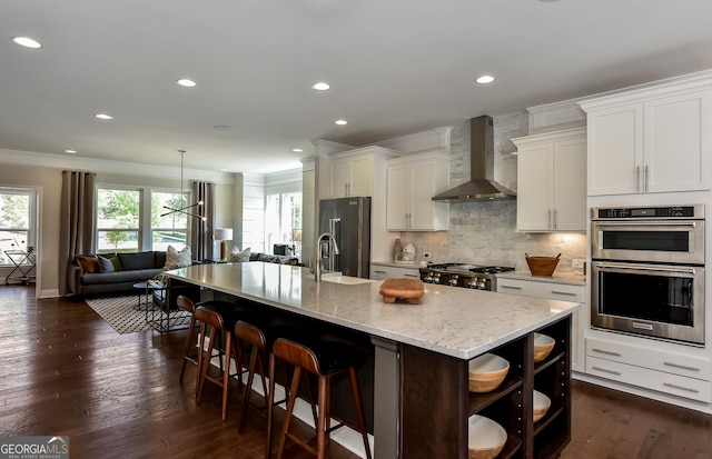 kitchen featuring white cabinetry, wall chimney range hood, an island with sink, and stainless steel appliances