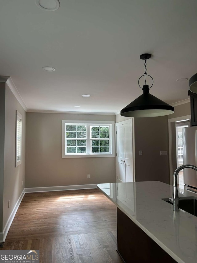 kitchen with sink, hanging light fixtures, light stone counters, stainless steel fridge, and crown molding