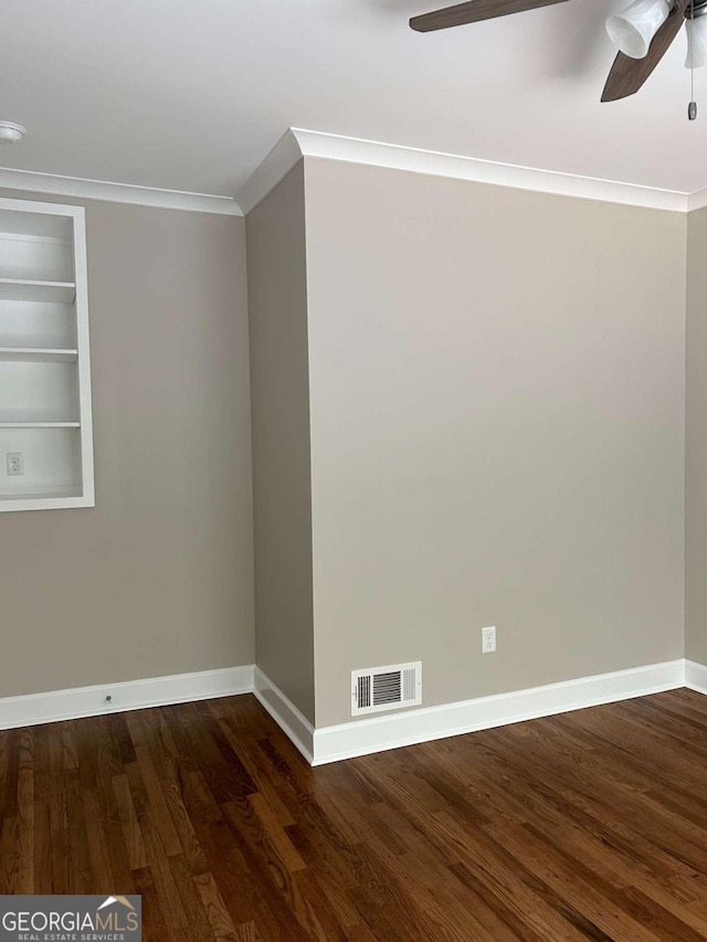 empty room featuring ornamental molding, built in features, ceiling fan, and dark wood-type flooring