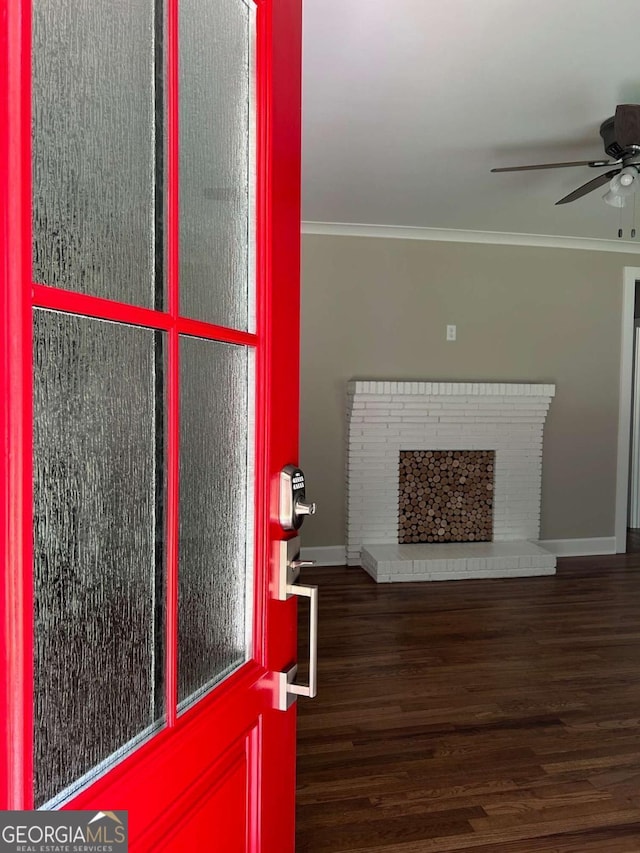 interior space with ceiling fan, ornamental molding, dark wood-type flooring, and a brick fireplace