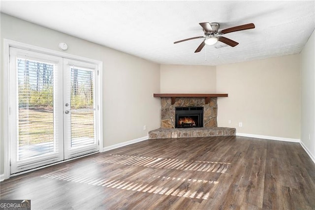 unfurnished living room with ceiling fan, a stone fireplace, dark hardwood / wood-style flooring, and french doors