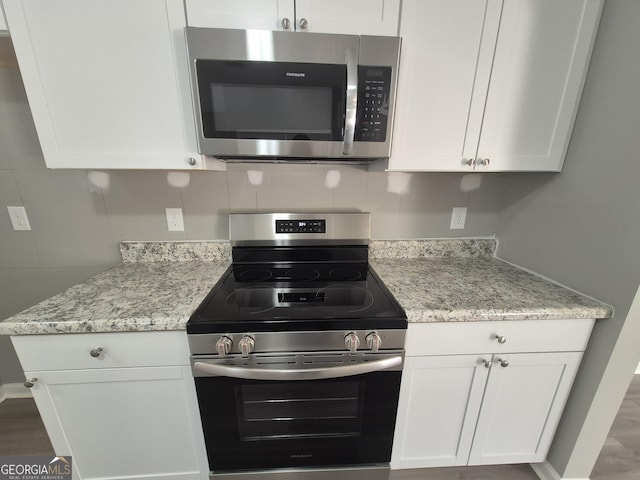 kitchen with white cabinetry, light stone counters, backsplash, appliances with stainless steel finishes, and hardwood / wood-style flooring