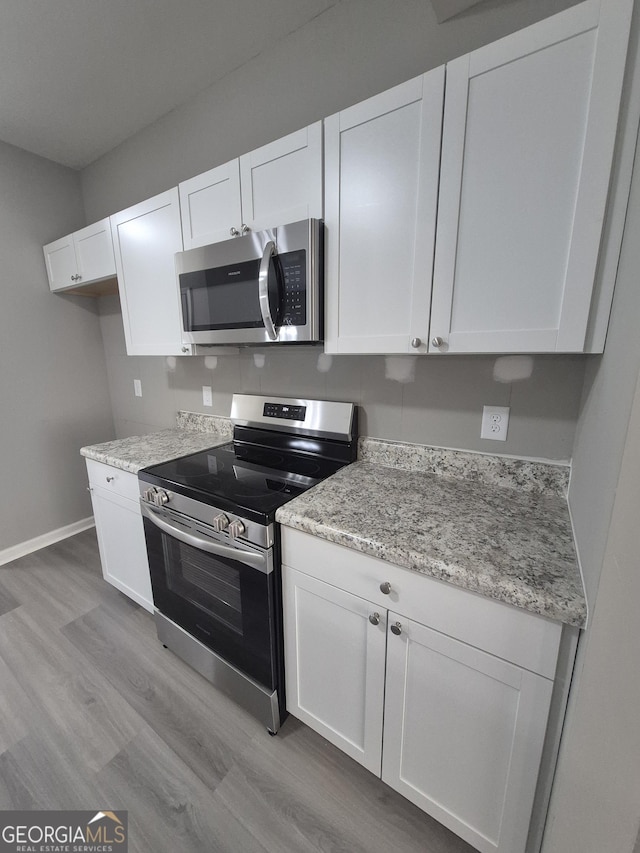 kitchen with white cabinets, appliances with stainless steel finishes, light hardwood / wood-style floors, and light stone counters