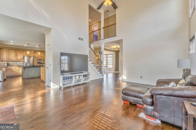 living room with a high ceiling, dark hardwood / wood-style flooring, ceiling fan, and ornamental molding