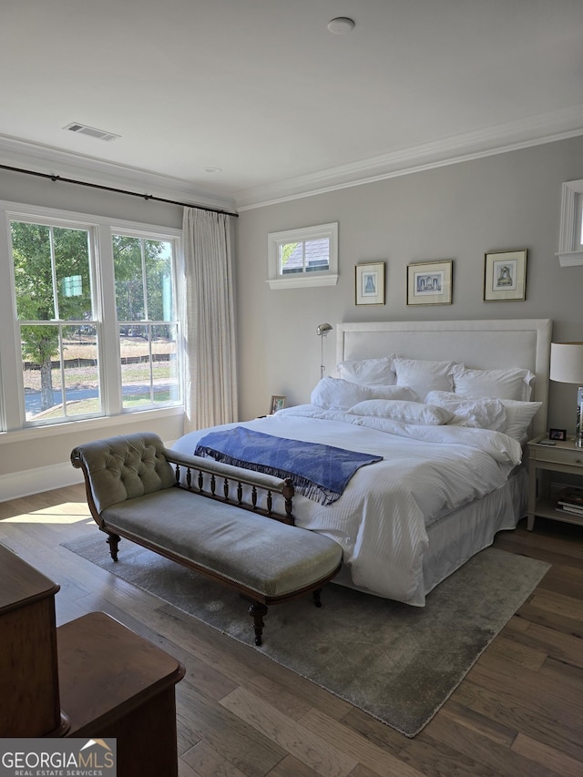 bedroom with multiple windows, visible vents, crown molding, and wood finished floors