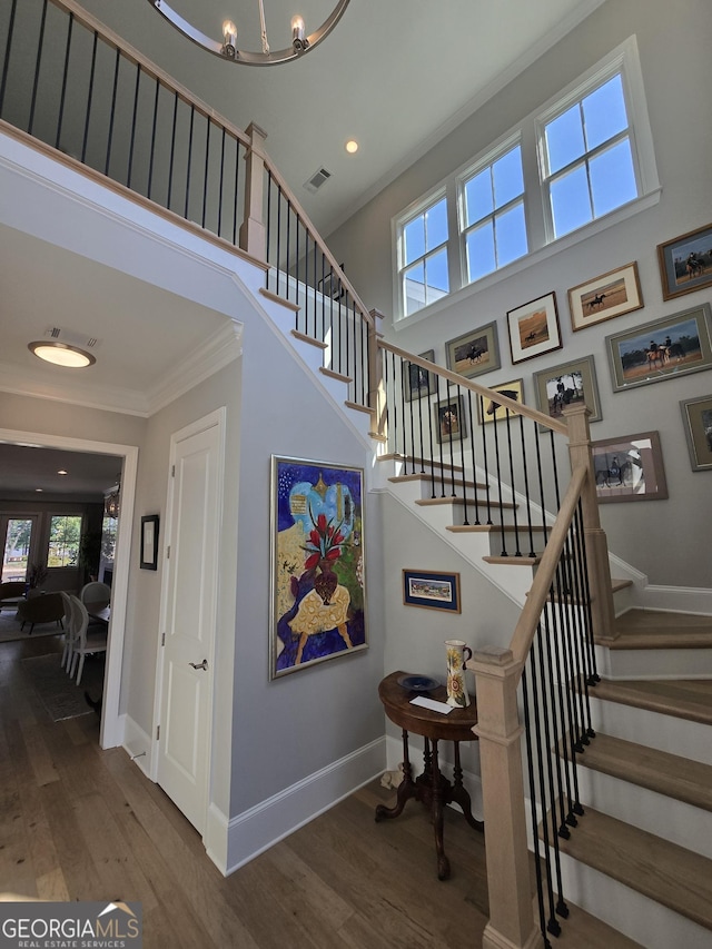 staircase featuring crown molding, a notable chandelier, and hardwood / wood-style flooring