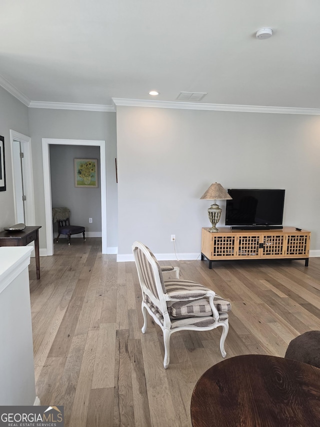 living area featuring hardwood / wood-style flooring, baseboards, visible vents, and ornamental molding