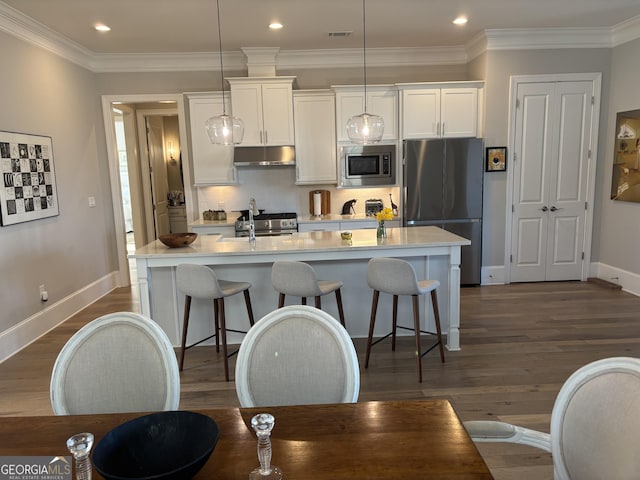 kitchen featuring tasteful backsplash, stainless steel appliances, under cabinet range hood, a kitchen bar, and white cabinetry