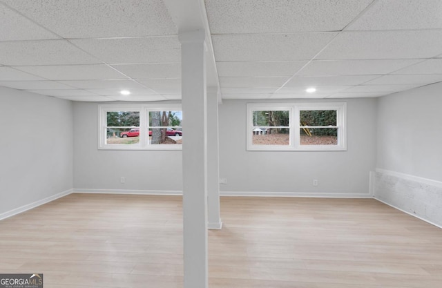 basement featuring a drop ceiling, a healthy amount of sunlight, and light wood-type flooring