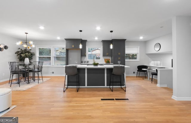 kitchen featuring gray cabinets, a chandelier, light hardwood / wood-style floors, hanging light fixtures, and a breakfast bar area