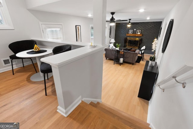 bar with ceiling fan, a fireplace, and light hardwood / wood-style flooring