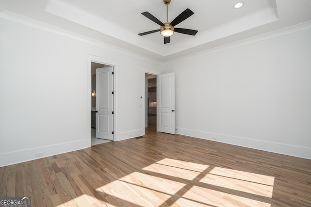 spare room featuring ornamental molding, a tray ceiling, wood finished floors, and baseboards