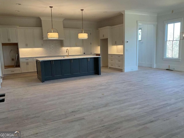 kitchen featuring decorative light fixtures, white cabinetry, and an island with sink