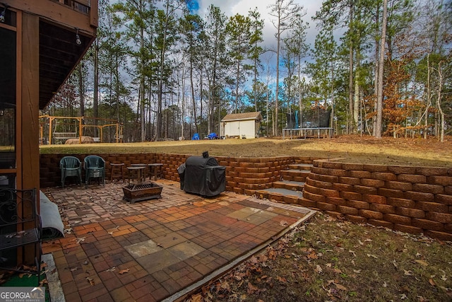 view of patio featuring a storage unit, a trampoline, an outdoor fire pit, and grilling area